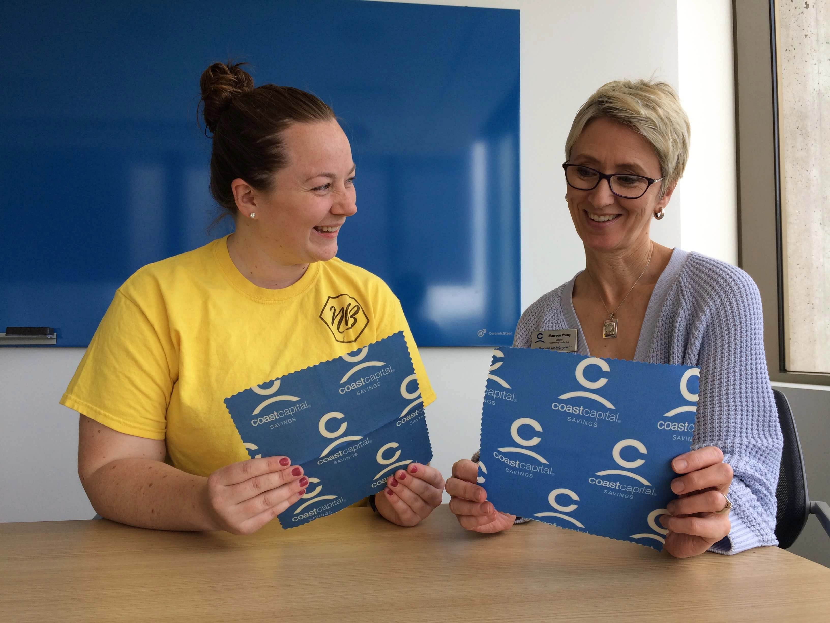Custom beeswax wraps for a corporate financial banking institution, coast capital. Beeswax wraps feature branded colours and logo on the custom product that is sustainable. Image shows nature bee founder Katie with the client from coast capital looking at the final customized product. 