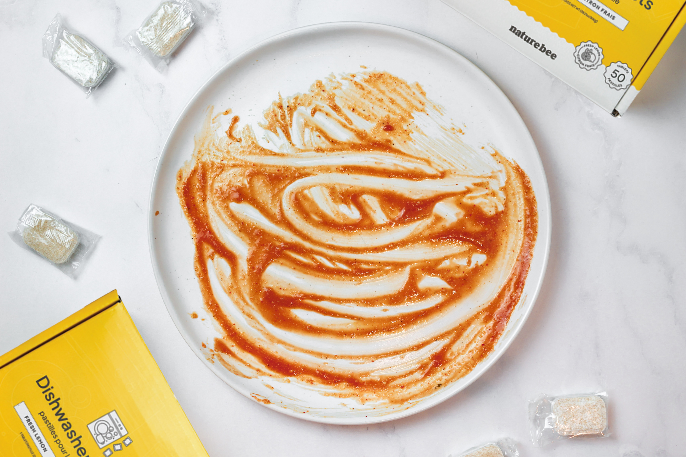 Comparison image 1: a white plate with tough red and yellow food stains from pasta sauce all over the plate