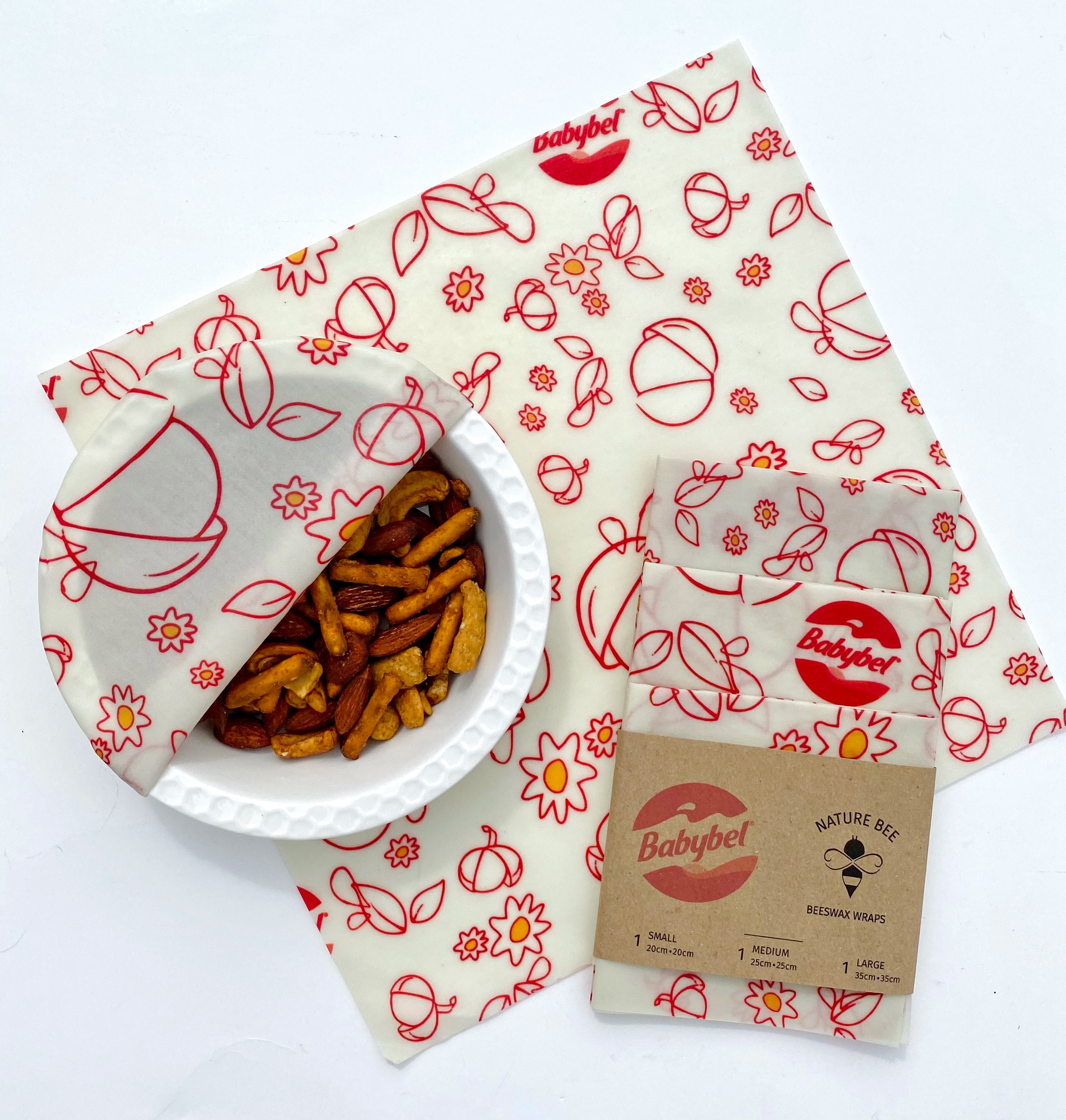 Babybel custom beeswax wraps for a corporate cheese company. One customized beeswax wraps with a white background and red icons and drawings include logos and artwork. Flat wrap on white counter with a bowl of pretzels wrapped in a beeswax wrap and a trio of three beeswax wraps packaged with a co-branded belly band. The perfect eco friendly way to spread the word about your brand. 