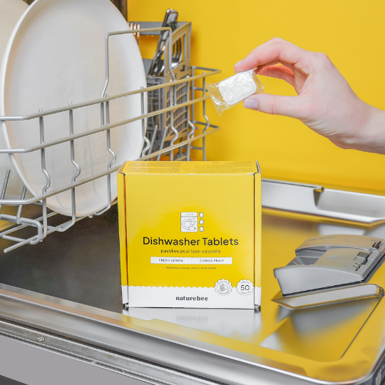 How to use dishwasher tablets image one shows a dishwasher with a bright yellow background. the yellow dish tab box is sitting on the open washer and a hand is holding one of the tablets